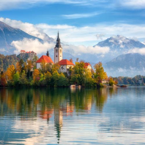 Famous alpine Bled lake (Blejsko jezero) in Slovenia, amazing autumn landscape. Scenic view of the lake, island with church, Bled castle, mountains and blue sky with clouds, outdoor travel background
