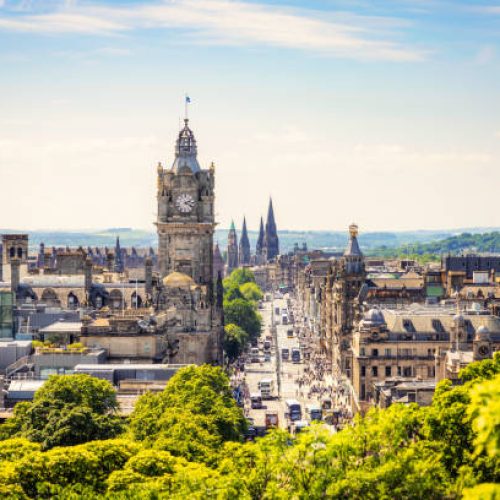 A high angle view over central Edinburgh, with Princes Street busy with pedestrians on a sunny afternoon.